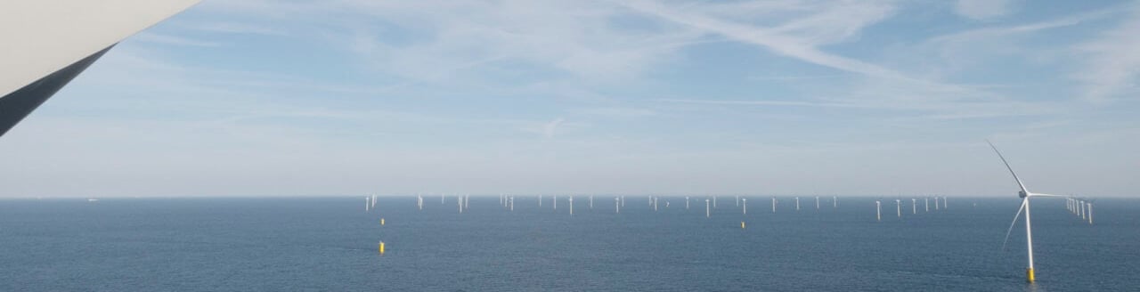 View from an offshore wind mill over the sea and more wind mills in the distance. The foreground includes the blade of a wind mill, framing the view.