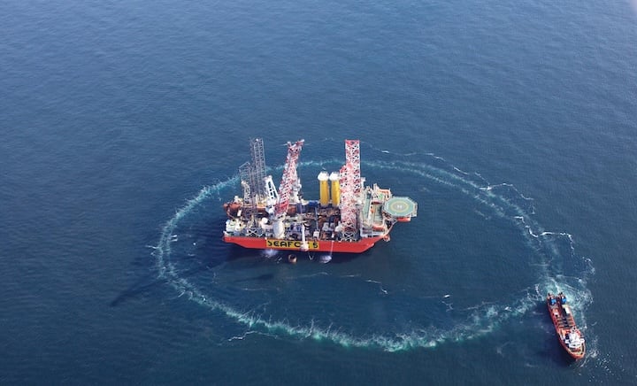 View from above over a wind mill building platform and a service boat making circles around it. View from above over a wind mill building platform and a service boat making circles around it.